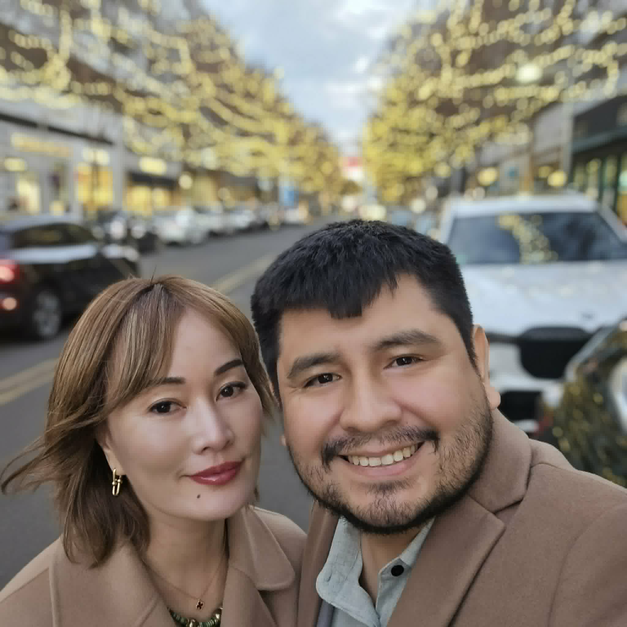 Smiling man and woman take a selfie on a city street with festive yellow lights.